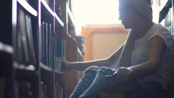 Young girl is sitting on the floor between rows of books — Stock Video