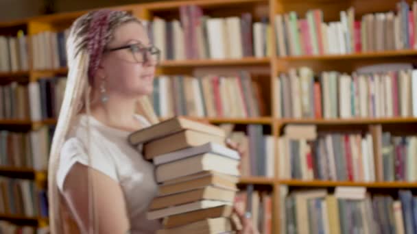 Hermosa rubia con libros en la biblioteca — Vídeo de stock