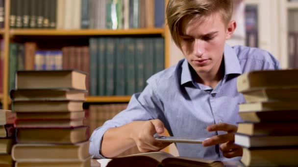 Junger hübscher Kerl am Tisch in der Bibliothek — Stockvideo