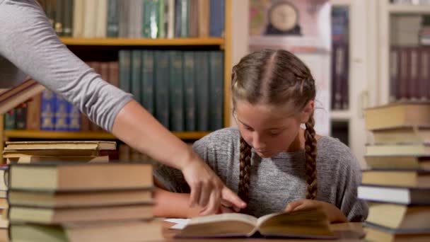 Liten flicka skriver vid ett bord i biblioteket — Stockvideo