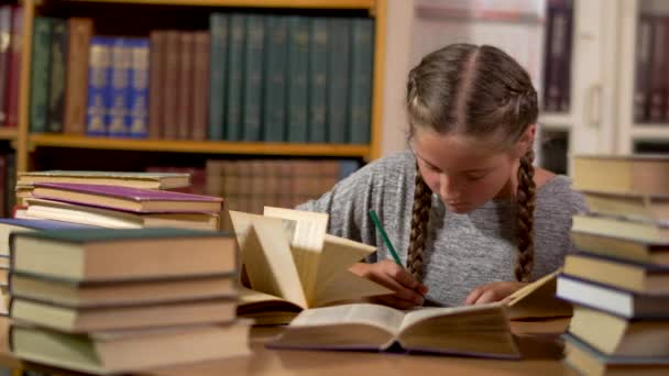 Niña escribe en una mesa en la biblioteca — Vídeos de Stock