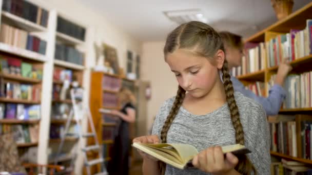 Niña con coletas en la biblioteca — Vídeos de Stock