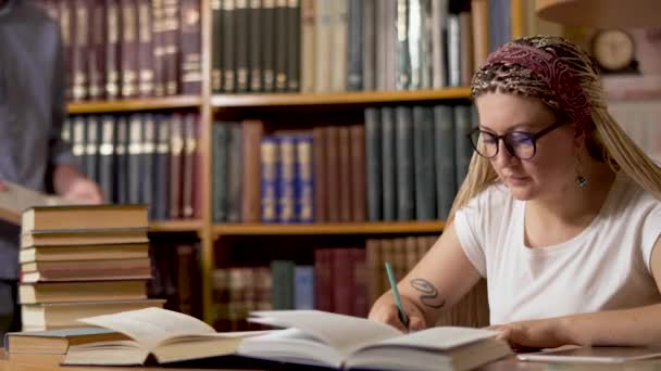 Hermosa chica está escribiendo en una mesa en la biblioteca — Vídeos de Stock