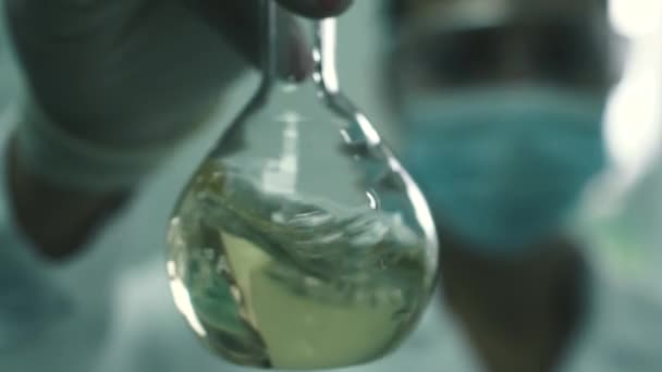 Laboratorní asistent dívka vyvolává kapalina v baňce — Stock video