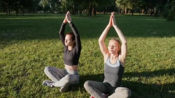 Två vackra flickor i sport leggings sitter i parken. — Stockvideo