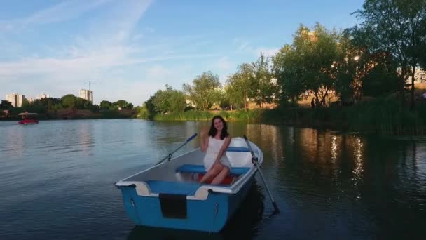 Hermosa chica está sentada en un barco en el lago y agitando sus brazos — Vídeos de Stock
