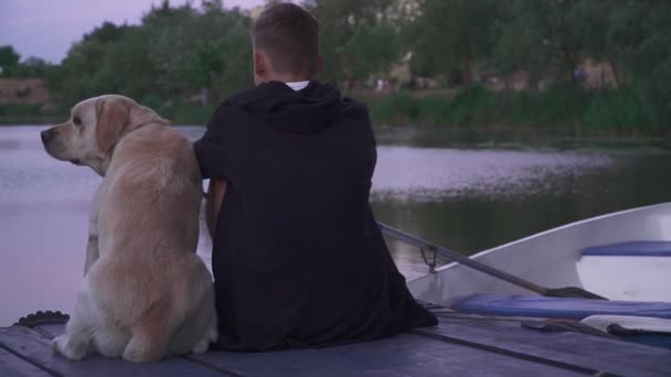 Joven con un perro en el muelle cerca del lago — Vídeos de Stock