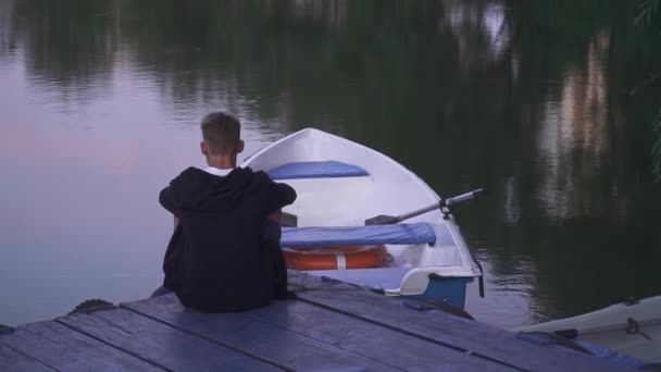Pohledný chlap sedí na doku nedaleko loď — Stock video