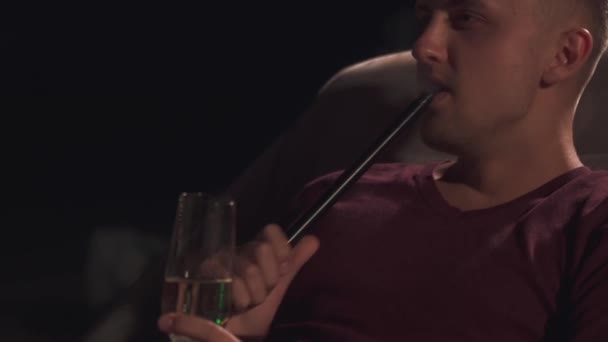 Jóképű srác, egy pohár pezsgővel tárolás és gőzölő egy vízipipa — Stock videók
