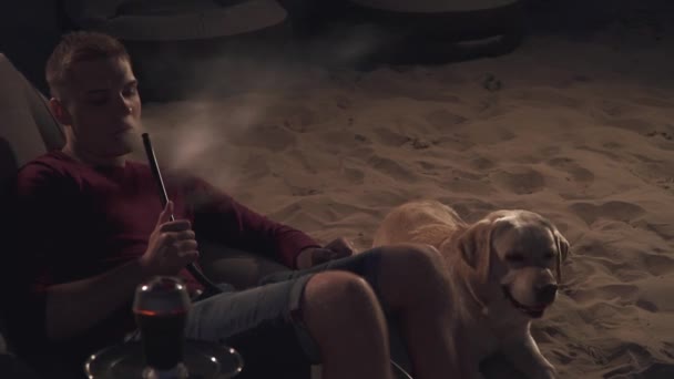 Guapo chico está descansando con un perro en la playa — Vídeo de stock