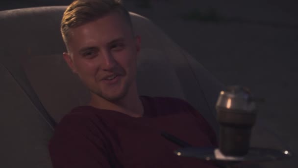 Young man sits in an armchair next to a hookah — Stock Video