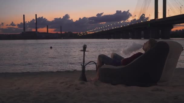 Jóképű srác dohányzik vízipipa a strandon — Stock videók