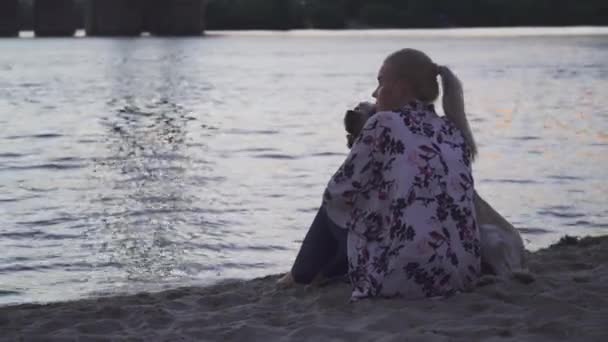 Mooi meisje zit met een hond op de rivier bank — Stockvideo