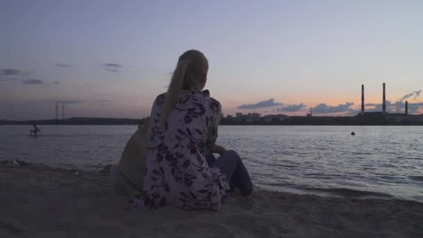 Bella ragazza è seduta con un cane sulla riva del fiume — Video Stock