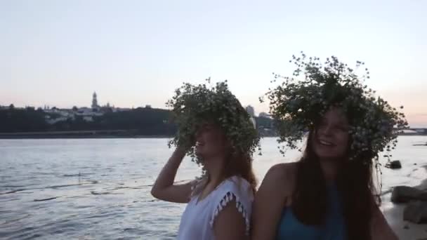 Две красивые девушки с венками на голове на берегу реки — стоковое видео
