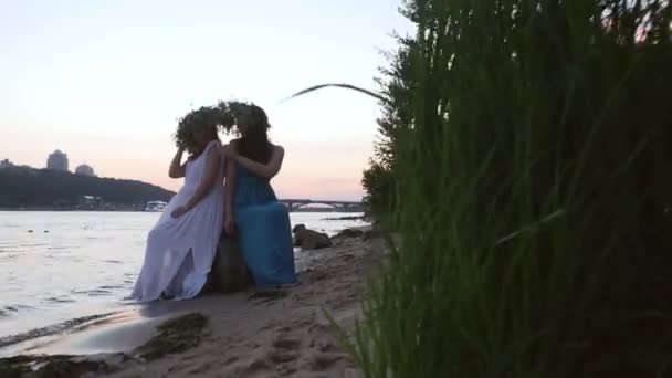 Twee mooie meisjes met kransen op het hoofd aan de rivieroever — Stockvideo