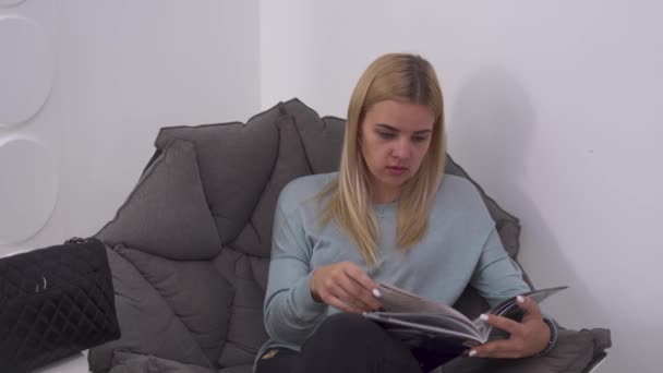 Güzel kız sandalye bir dergide başparmak — Stok video