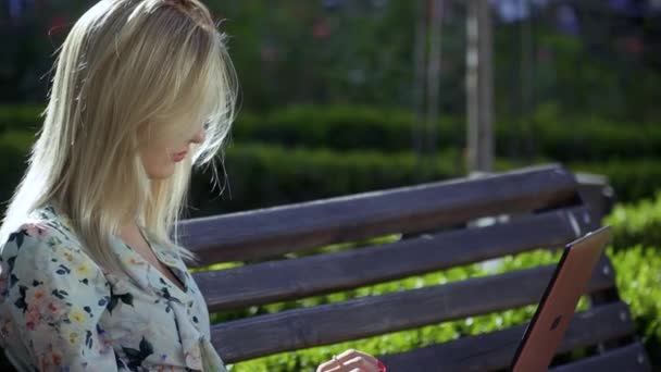 Schönes Mädchen sitzt auf einer Bank im Park — Stockvideo