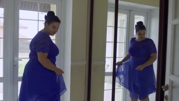 Menina gorda em um vestido azul na frente de um espelho — Vídeo de Stock