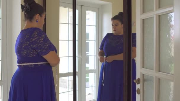 Dik meisje in een blauwe jurk voor een spiegel — Stockvideo