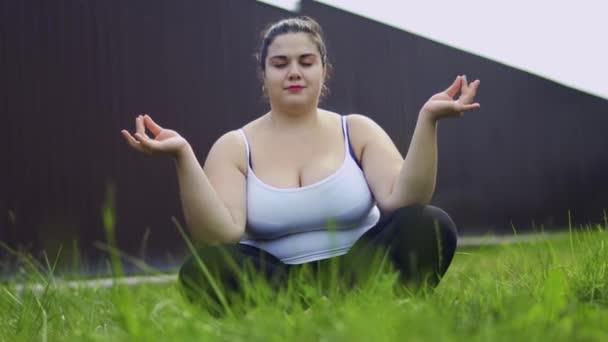A menina gorda senta-se na grama e medita — Vídeo de Stock