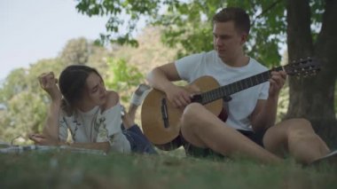 Genç adam ve kadın şarkı oluşturun. Çocuk gitar çalıyor ve kız metin yazma. Yaratıcı gençlik açık havada dinlenme