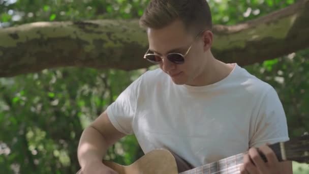 Ung man spelar gitarr i trädgården — Stockvideo