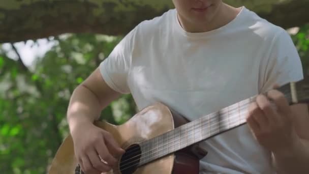 Ung man spelar gitarr i trädgården — Stockvideo