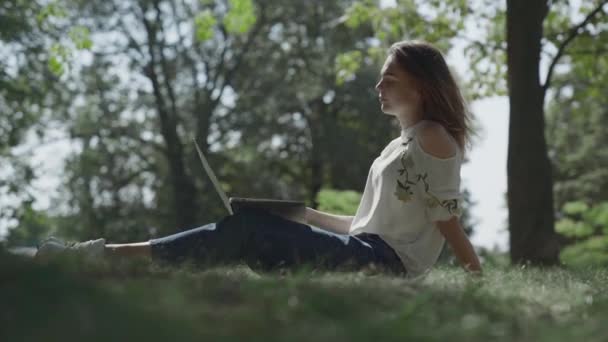 Молодая девушка сидит с ноутбуком на открытом воздухе — стоковое видео