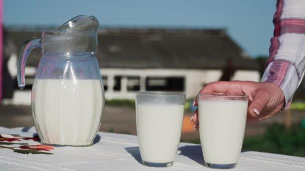 女性の手は テーブルからミルク ガラスを取ります つのグラスで透明な水差しは外のテーブルで 健康的な田舎のライフ スタイル クローズ アップ — ストック動画