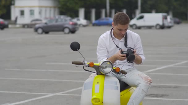 那家伙坐在滑板车上拍了张照片穿着黄色复古轻便摩托车的白色衬衫的帅哥骑滑板车 — 图库视频影像