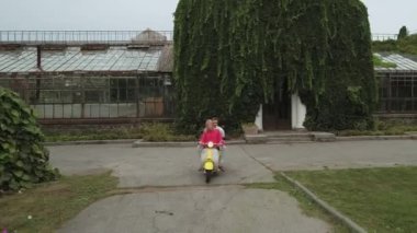 Güzel çift parkta bir scooter sürme. Genç çift açık havada bir motosiklet sürüş. Kız bir scooter tekerlekli adam. Drone çekim.