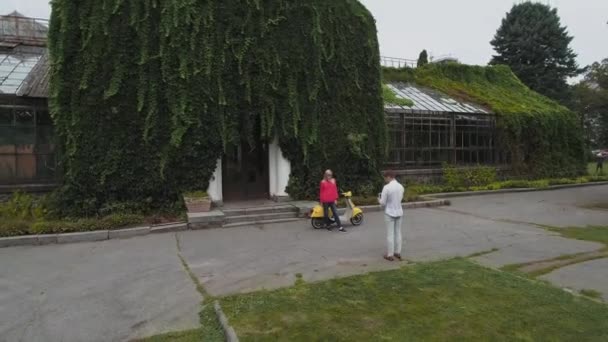 若いカップルは スクーターの近くを抱き締めます スクーターに近いポーズ美しい少女 ヤング カップル公園の家の近くのスクーター ドローンから撮影 — ストック動画