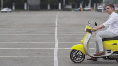 Adam scooter üzerinde park yerinde sürüş başlar. Genç adam bir motosiklet Binme. Yakışıklı bir motosiklet sürme beyaz gömlekli olan. Genç adam bir sarı retro motor bisiklet.