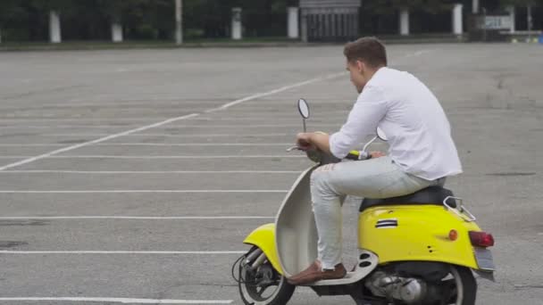 年轻的家伙在停车场骑摩托车 骑摩托的年轻人 穿着白色衬衫的帅哥骑摩托车 年轻的家伙在一个黄色的复古汽车自行车 — 图库视频影像
