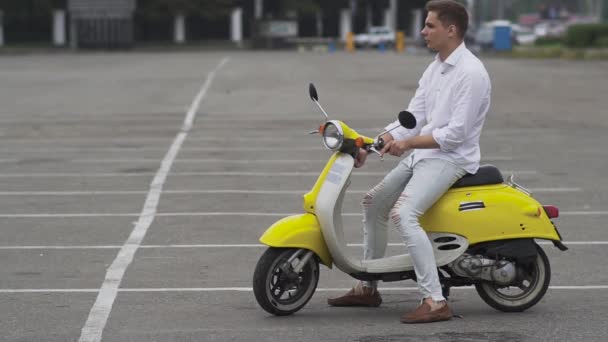 年轻人关掉引擎 把滑板车留在停车场 穿着白衬衫的帅哥离开了滑板车 年轻的家伙在一个黄色的复古汽车自行车 — 图库视频影像