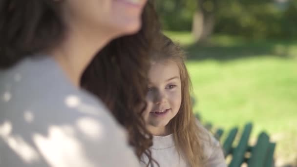 Mamãe e sua filhinha estão descansando em um banco no parque — Vídeo de Stock