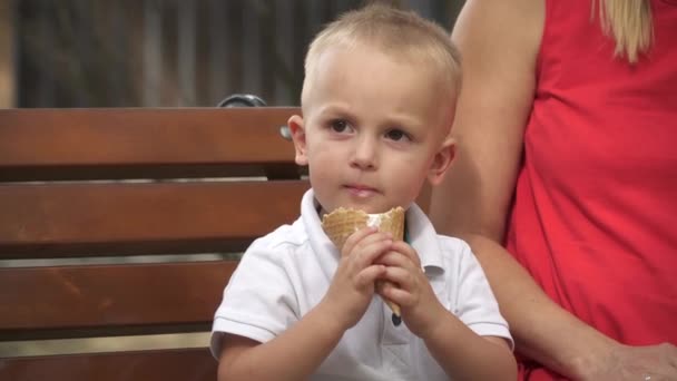 Χαμογελώντας μικρό αγόρι τρώει παγωτό σε ένα παγκάκι — Αρχείο Βίντεο