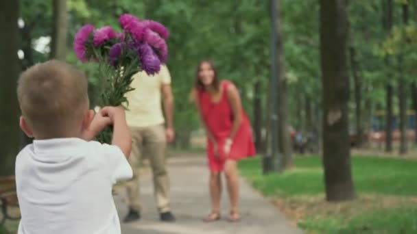 Мальчик бегает с цветами к родителям — стоковое видео