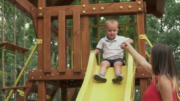 Mama hält die Hand eines kleinen Jungen, der auf einer Kinderrutsche sitzt — Stockvideo