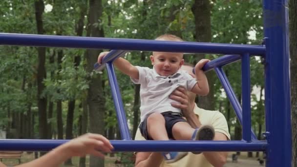 Parents next to a child standing on a horizontal bar in the park — Stock Video