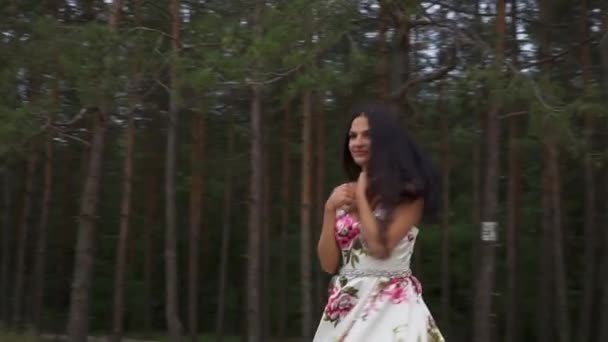 Vacker flicka i en lång klänning snurrar mot bakgrund av skogen — Stockvideo