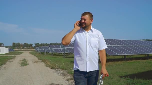 Бизнесмен разговаривает по телефону на фоне солнечных батарей — стоковое видео