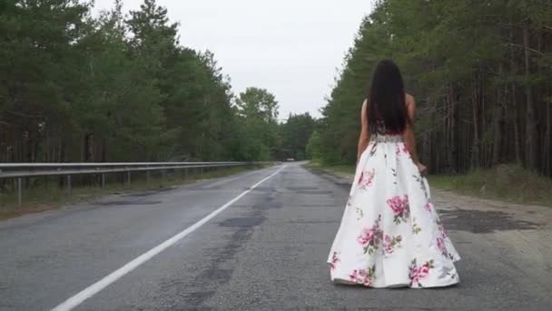 Menina bonita em um vestido longo e bonito caminha na estrada — Vídeo de Stock