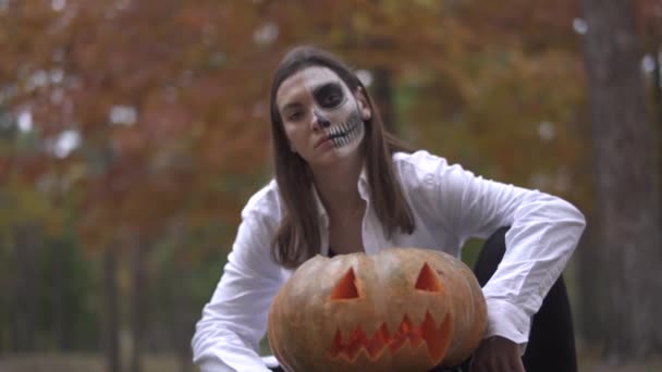 Halloween. Una chica con un maquillaje de Halloween aterrador está sentada cerca de la calabaza — Vídeos de Stock