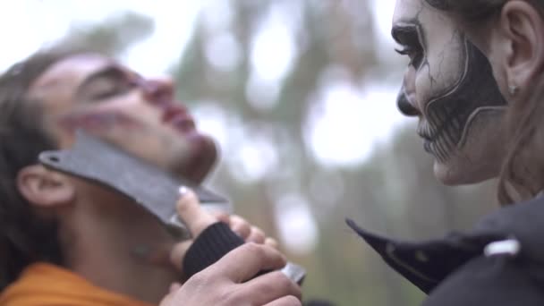 Halloween. Mujer aterradora con un maquillaje terrible amenaza al tipo con un cuchillo — Vídeos de Stock