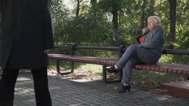 Een volwassen man benaderingen een vrouw zitten op een bankje — Stockvideo