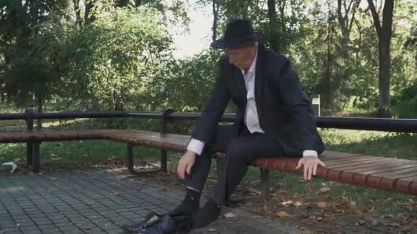 Vieil homme ivre enlève ses chaussures et s'allonge sur le banc — Video