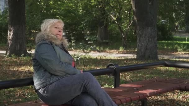 成熟的女人在公园里等着坐在板凳上 金发女郎喜欢她的时间户外 女人在微笑 — 图库视频影像