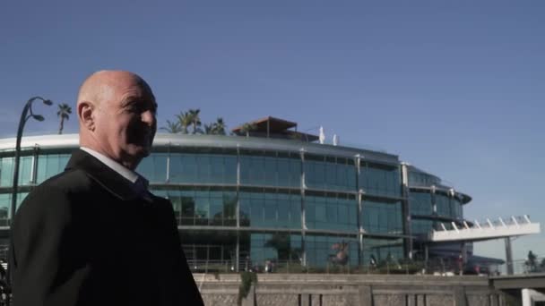 Vieil homme dans un manteau strict sur le fond d'un bâtiment moderne — Video